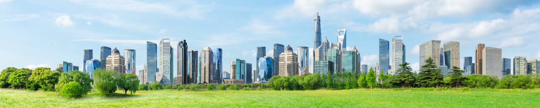 A panoramic view of a modern city skyline with a lush green park in the foreground under a blue sky.